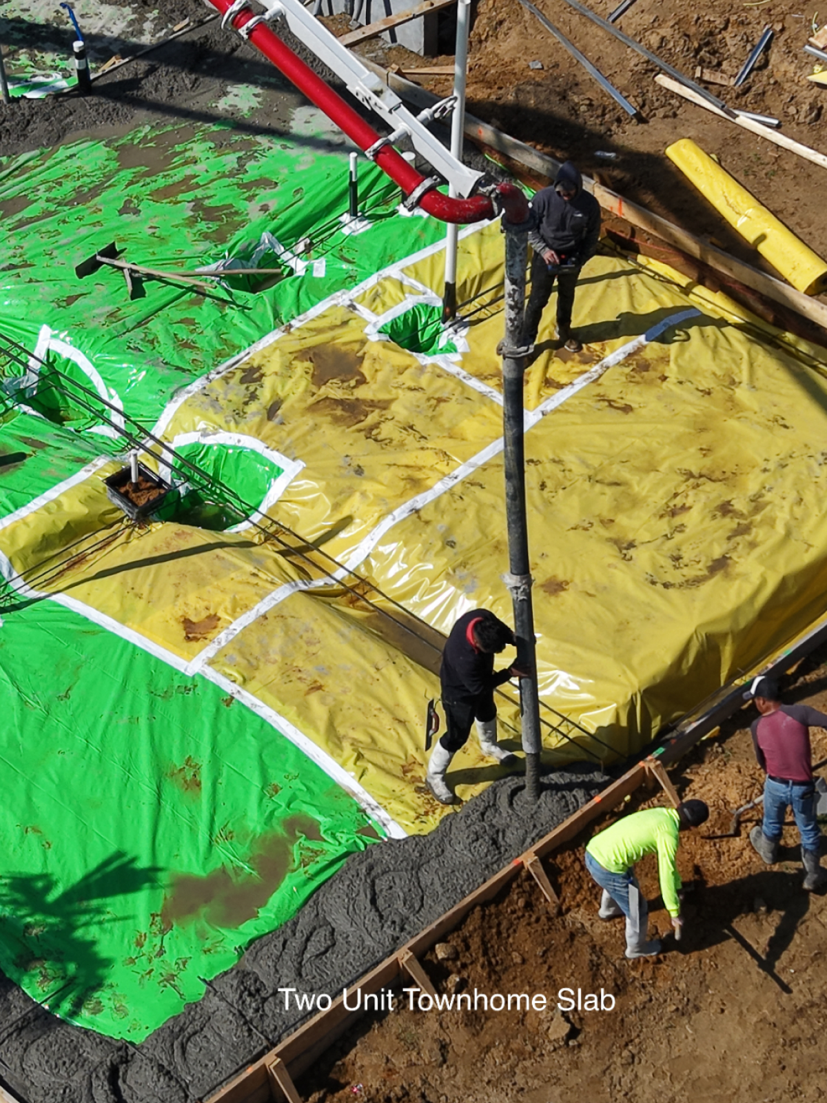 Construction workers pour concrete onto a two-unit townhome slab with green and yellow vapor barriers.